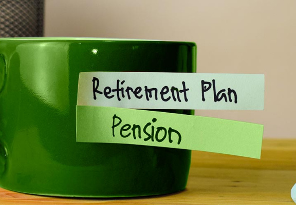 Cup of coffee on top of desk with sticky notes reading, retirement plan and pension.